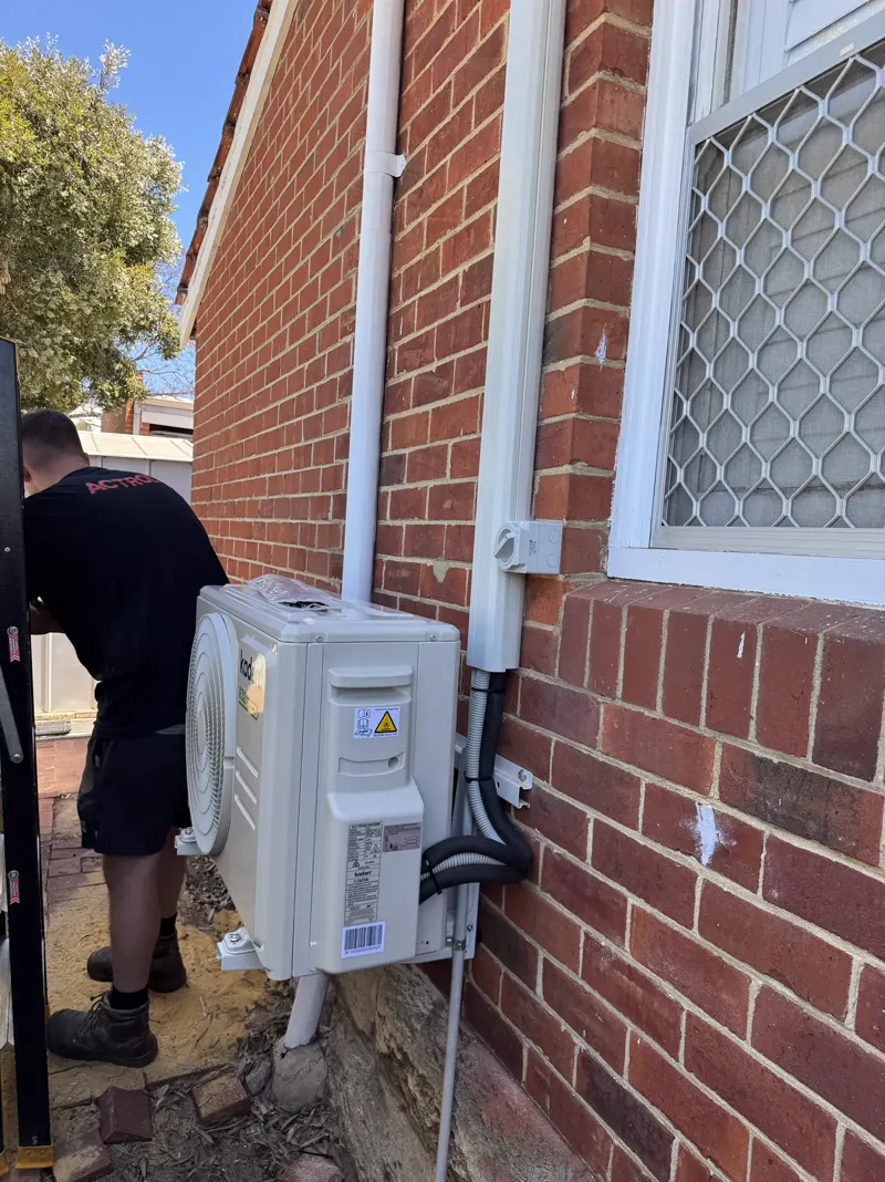 Calabreeze technician installing an outdoor air-conditioning unit at a red brick Perth home