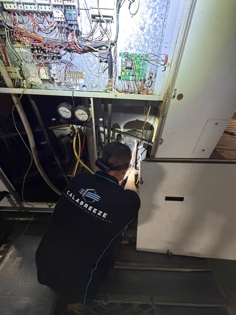 Calabreeze technician servicing a rooftop air-conditioning unit with refrigerant gauges