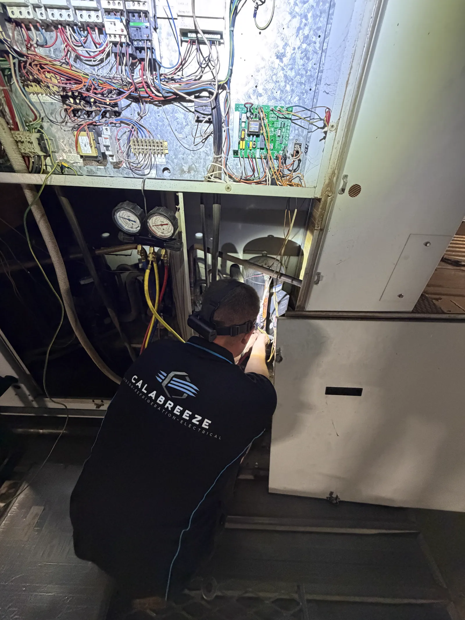 Calabreeze technician servicing a rooftop air-conditioning unit with refrigerant gauges in Perth