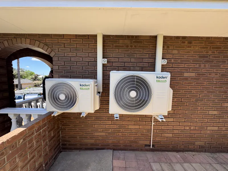 Two split system condensers wall-mounted on brick at a Perth home